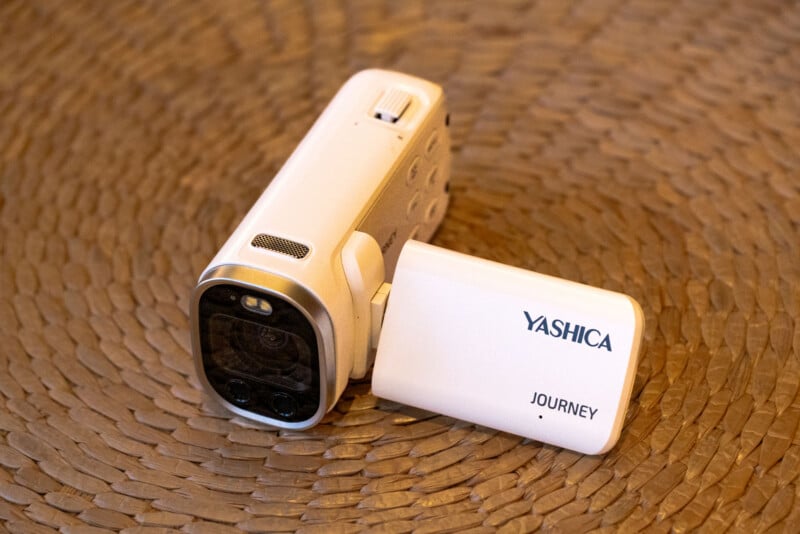 A white Yashica Journey camcorder with its LCD screen flipped open, resting on a woven, textured brown surface.