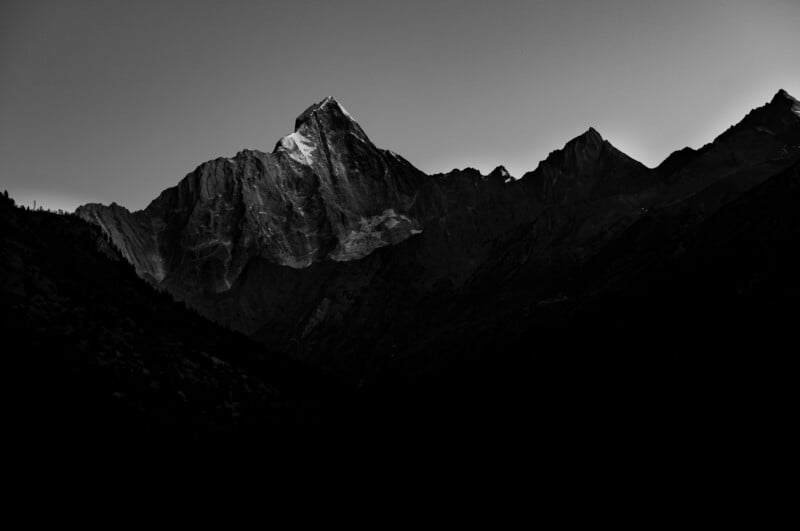 Una sorprendente fotografía en blanco y negro de un escarpado pico montañoso iluminado por la luz del sol, con crestas afiladas y sombras oscuras en primer plano y al fondo.