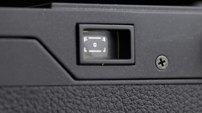 Close-up of a camera viewfinder, showing frame lines and focus indicators inside, with a textured black camera body and a visible screw nearby.