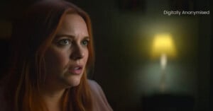 A woman with long red hair looks concerned in a dimly lit room. The background is blurred with a glowing lamp, and the words "Digitally Anonymised" appear in the top right corner.