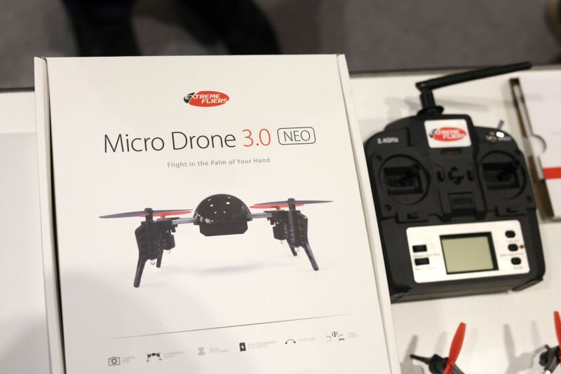 Se muestra el kit Micro Drone 3.0 NEO en caja de Extreme Fliers, que muestra una imagen del dron en la caja, así como un controlador con una pantalla LCD y controles etiquetados en una superficie blanca al lado de ellos.