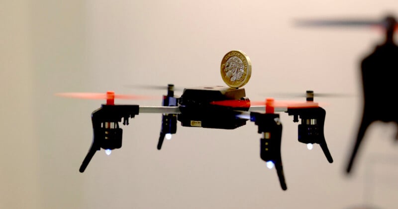 Un pequeño dron con una hélice con punta roja vuela en el interior, con una moneda encima. El fondo está desenfocado, resaltando el dron y las monedas.