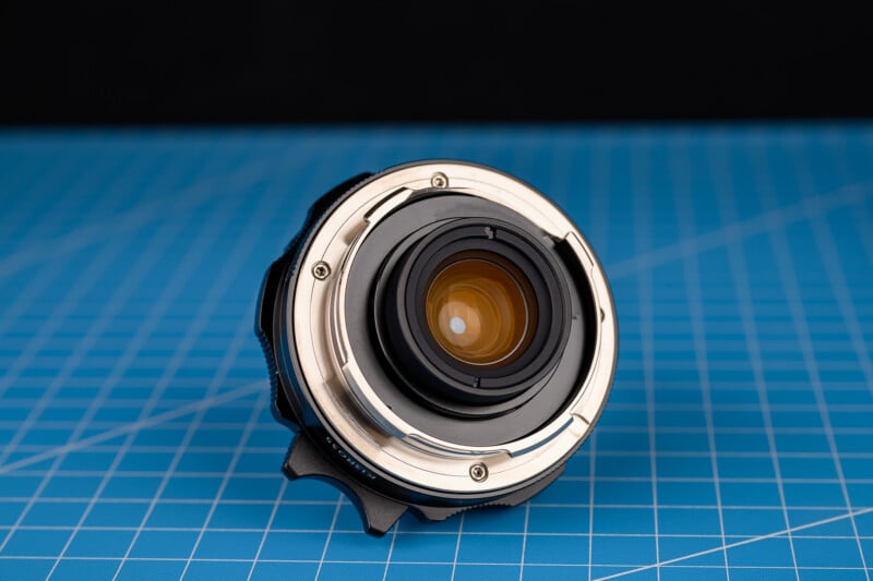 La lente de la cámara se coloca boca arriba sobre una superficie con patrón de cuadrícula azul con un fondo negro detrás.