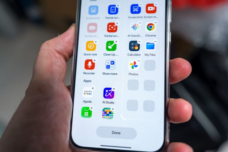 A hand holds a smartphone displaying several app icons on the screen, including Recorder, AI Studio, Agoda, Photos, Chrome, and Calculator. The phone shows app folders and a “Done” button at the bottom.