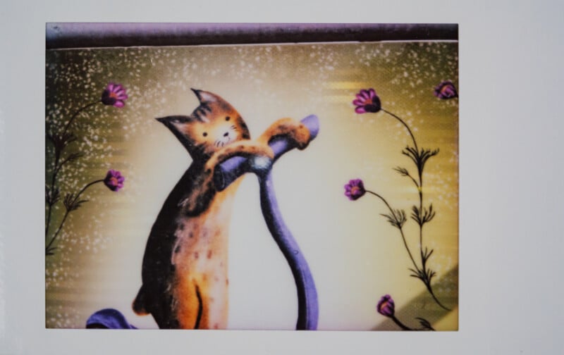 Una ilustración caprichosa de un gato sosteniendo un objeto curvo rodeado de pequeñas flores de color púrpura sobre un fondo con textura amarilla.