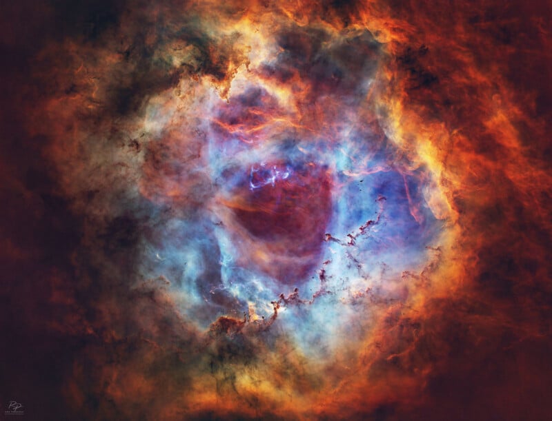 Una nebulosa brillante y colorida en el espacio con nubes arremolinadas de gas azul, rojo, naranja y amarillo que forman un círculo con un centro oscuro rodeado de una luz brillante y vibrante.