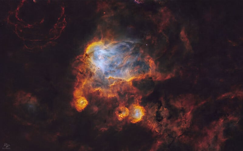 Nebulosa brillante y colorida con brillantes nubes de gas y polvo de color naranja, amarillo y azul sobre un fondo oscuro y moteado de estrellas del espacio profundo.