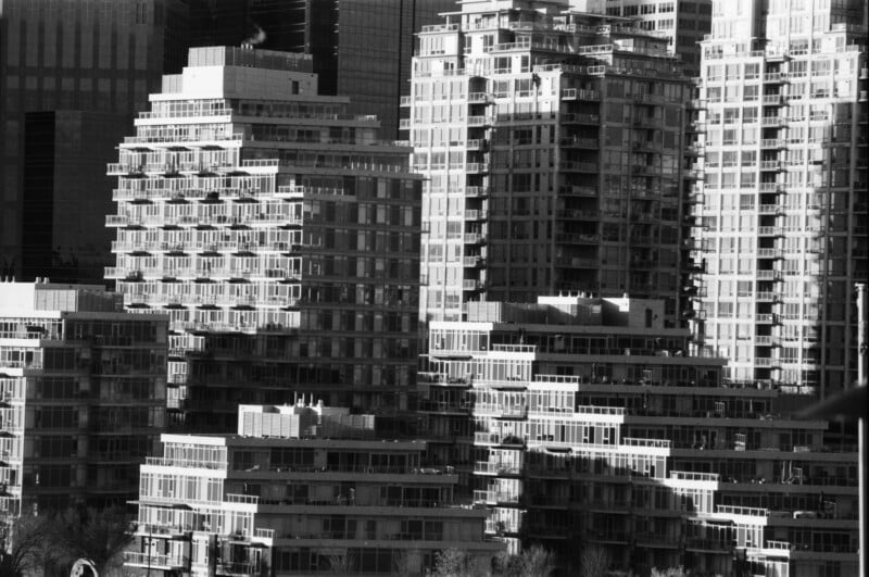 Black and white photo of modern high-rise apartment buildings with numerous balconies, closely packed together, casting geometric shadows on each other in an urban setting.