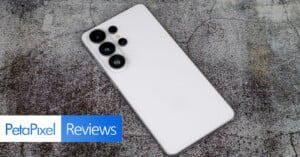 A white smartphone with multiple rear cameras lies on a textured gray surface. At the bottom left, the words "PetaPixel Reviews" appear in a white and blue banner.