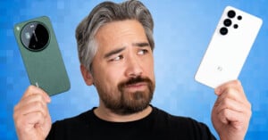 A man with gray hair and beard holds a green smartphone in his left hand and a white smartphone in his right hand, looking thoughtfully at the devices against a blue pixelated background.