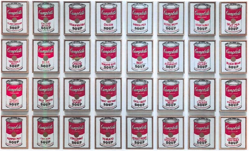 A grid of 32 Campbell’s Soup cans, each labeled with a different flavor, arranged in four rows and eight columns against a white background. The cans are depicted in a pop art style.