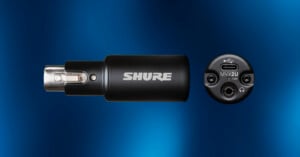 Black Shure audio adapter shown from the side with logo visible and from the end, displaying XLR, USB-C, and headphone ports against a blue gradient background.
