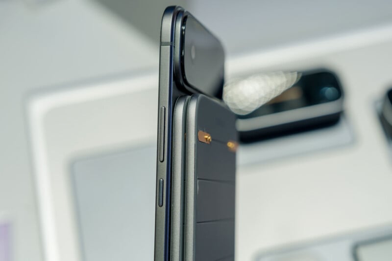 Primer plano de la vista lateral de dos teléfonos inteligentes modernos (uno negro y otro gris oscuro) que muestran sus botones y módulos de cámara con un fondo tecnológico borroso.