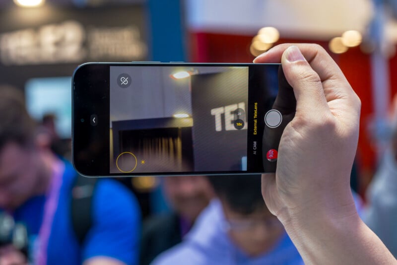 Sosteniendo un teléfono inteligente en una mano y usando la cámara para enfocar el letrero del edificio mientras las personas en el fondo están borrosas y desenfocadas.