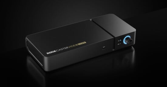 A black rectangular audio device labeled "RODECASTER VIDEO CORE" with a blue-lit knob, buttons, and vents, set against a dark background.