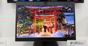 A computer monitor displays a vibrant image of a snowy Japanese shrine with red torii gates illuminated at night, people walking under the gates, and snow-covered trees surrounding the scene.
