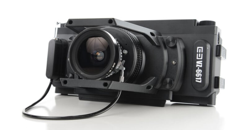 A black, boxy medium format camera with a prominent lens and a cable attached, labeled "VZ-6611" on the side, positioned on a white surface.