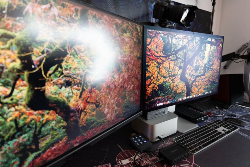 A desktop setup with two monitors displaying autumn forest scenes, a Mac Studio computer, keyboard, mouse, camera mounted on top of a monitor, and various tech accessories on a desk mat.