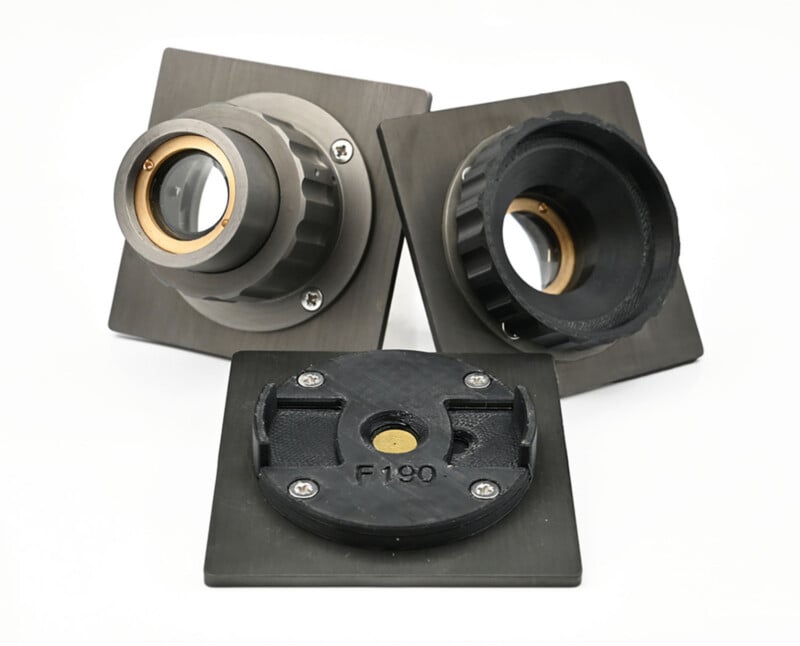 Three metallic and black components with circular openings, set on square plates, are arranged on a white surface. One component shows the label "F190" on its base.