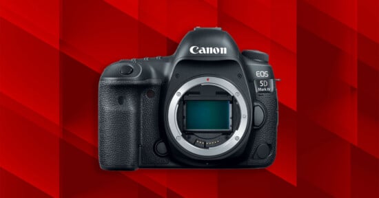 A black Canon EOS 5D Mark IV DSLR camera body with no lens attached, shown against a geometric red background.