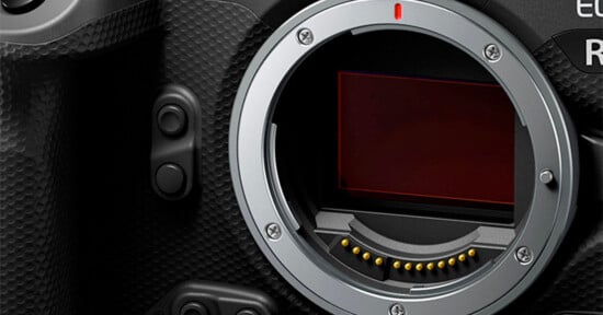 Close-up of a digital camera body showing the lens mount and exposed image sensor, with textured grip and control buttons visible on the left side.