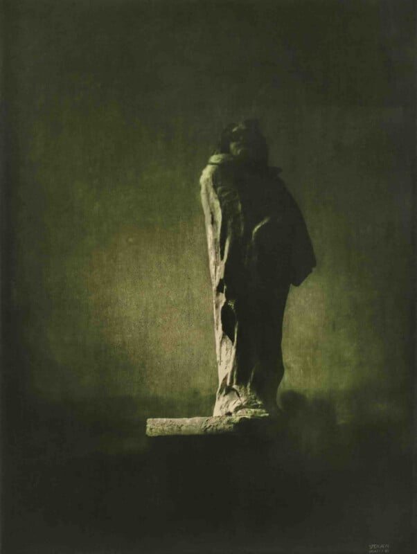 A statue of a standing figure in a long robe is illuminated by soft, moody light against a dark, textured background, creating a dramatic and mysterious atmosphere.