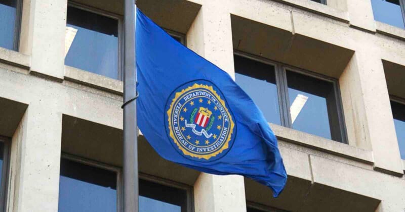Una bandera azul con el sello del FBI ondeaba en un asta frente a un edificio de oficinas de color beige con grandes ventanales.