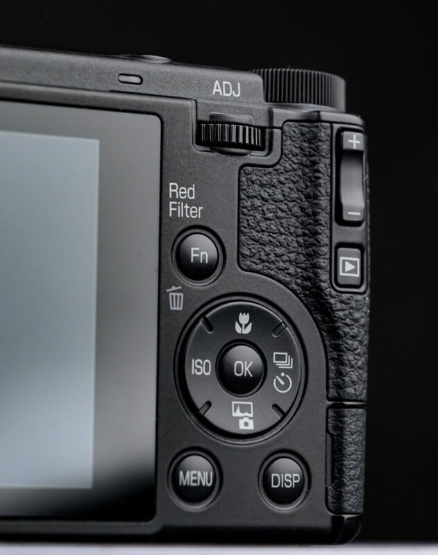 Close-up of the back controls of a digital camera, showing a textured grip, adjustment dial, buttons labeled MENU, DISP, ISO, Fn, and directional controls next to the display screen.