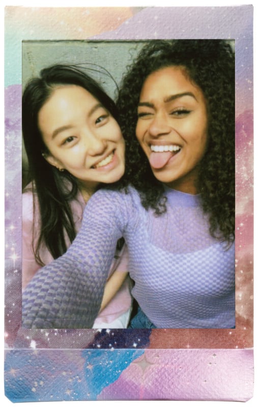 Dos mujeres jóvenes sonríen para una selfie, una de ellas saca la lengua en broma. Ambos vestían blusas moradas. Esta foto tiene un borde colorido, pastel y con temática de galaxias.