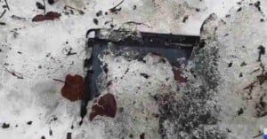 A partially frozen black laptop is embedded in melting ice and snow, surrounded by scattered brown leaves and small twigs.