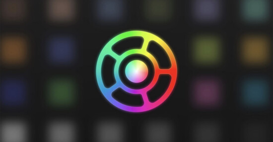 A circular logo with a black center and radiating segments, outlined in a gradient of bright rainbow colors, set against a blurred dark background featuring faint colored squares.