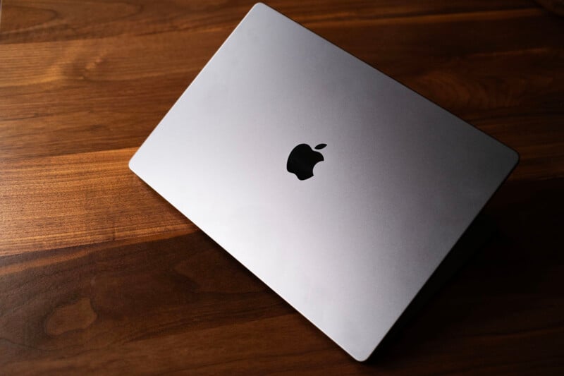 A partially closed silver Apple MacBook sits on a dark wooden surface, displaying the black Apple logo on the lid.