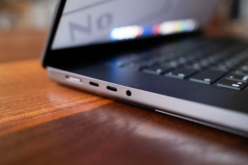 Close-up of a laptop's side, showing USB-C ports, a headphone jack, and part of the keyboard and screen, resting on a wooden surface.