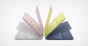 Four Apple MacBook laptops in pink, yellow, silver, and blue are arranged in a circle, each partially open with keyboards visible, creating a symmetrical, star-like pattern on a white background.