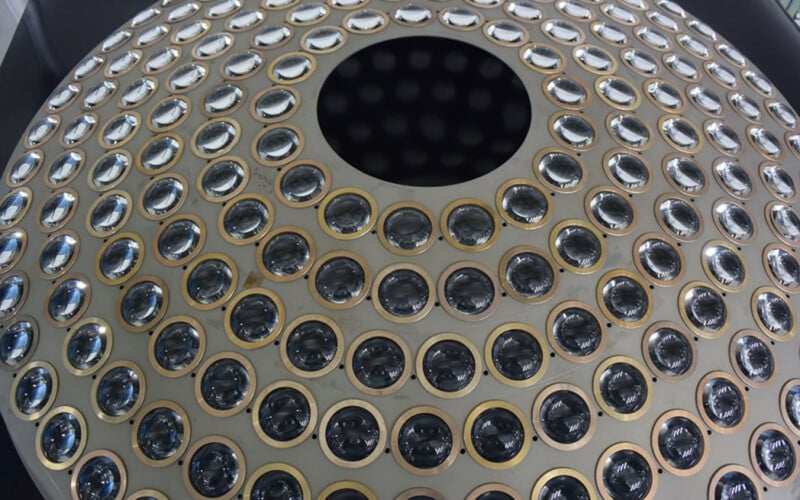 A large, circular metallic structure with concentric rings of evenly spaced, round glass or lens-covered openings, and a central black hole at the top.