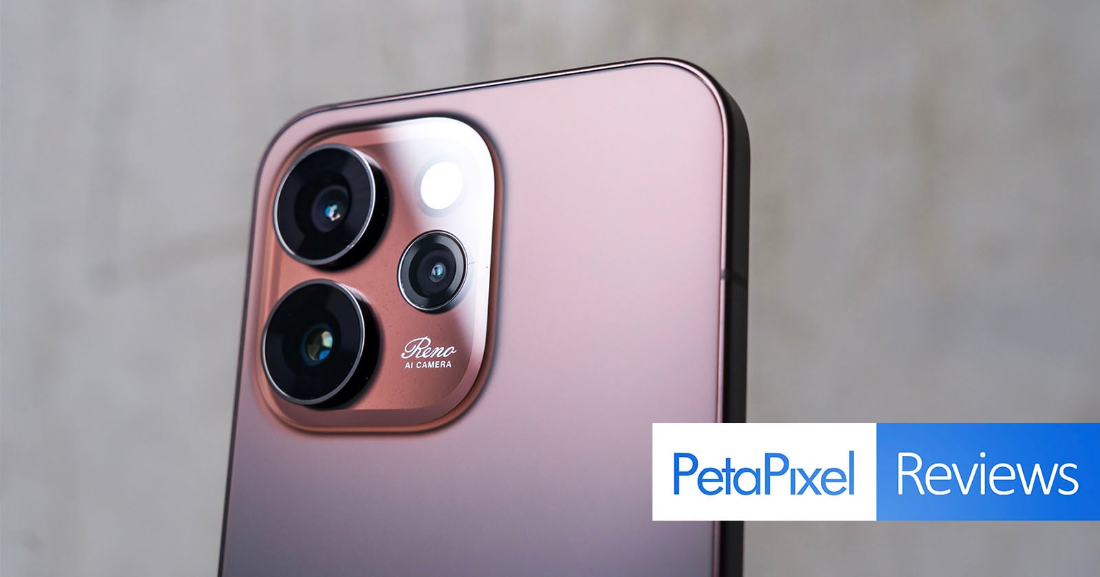 A close-up of a rose gold smartphone’s rear camera module with three lenses and a flash. The words “Reno AI Camera” are engraved. The Petapixel Reviews logo appears at the bottom right corner.
