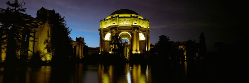 The Palace of Fine Arts in San Francisco illuminated at night, with its reflection shimmering in the water and a dark sky in the background.