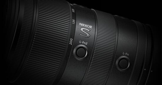 Close-up of a black Nikkor S camera lens, showing detailed texture, focal length markings (135, 200), and two customizable L-Fn buttons on the lens barrel against a dark background.