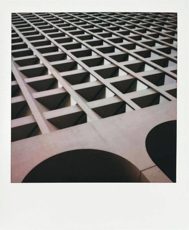 La fachada en forma de cuadrícula del edificio moderno, vista desde un ángulo desde abajo, con aberturas cuadradas repetidas y dos grandes recortes circulares en primer plano. La imagen tiene un tono ligeramente retro.