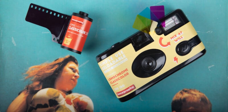 A disposable Lomography camera, a roll of Lomochrome film, and three color gel filters rest on a blue surface featuring a faded image of a woman and child.
