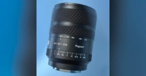 A close-up of a black camera lens labeled "Thypoch 24-50/2.8" against a blue background, showing detailed focus and aperture markings.