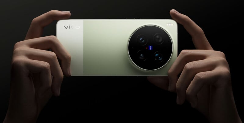 A person holding a light green Vivo smartphone horizontally, showing the back with a large black circular camera module and three lenses against a dark background.
