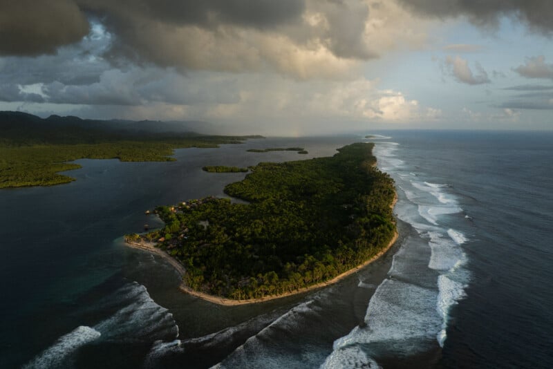 Aerial view of a lush, green peninsula surrounded by ocean waves, with dense forests, small coastal settlements, and dramatic clouds casting shadows over the landscape.