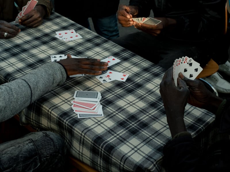 Four people playing cards at a table covered with a checkered cloth. Three hands are visible holding cards, while one person is reaching towards the center, where cards are laid face up.