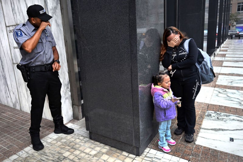 A security guard stands nearby as a distressed woman covers her face, while a young girl in a purple jacket leans against a building, holding a snack, both appearing upset.