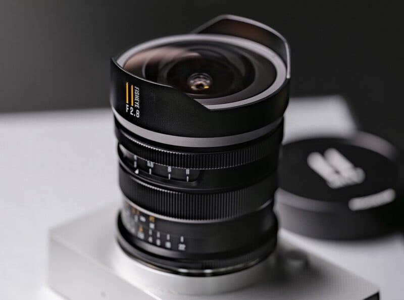 Primer plano de la lente de la cámara gran angular con parasol en forma de pétalo montado en el cuerpo plateado de la cámara. La lente muestra 