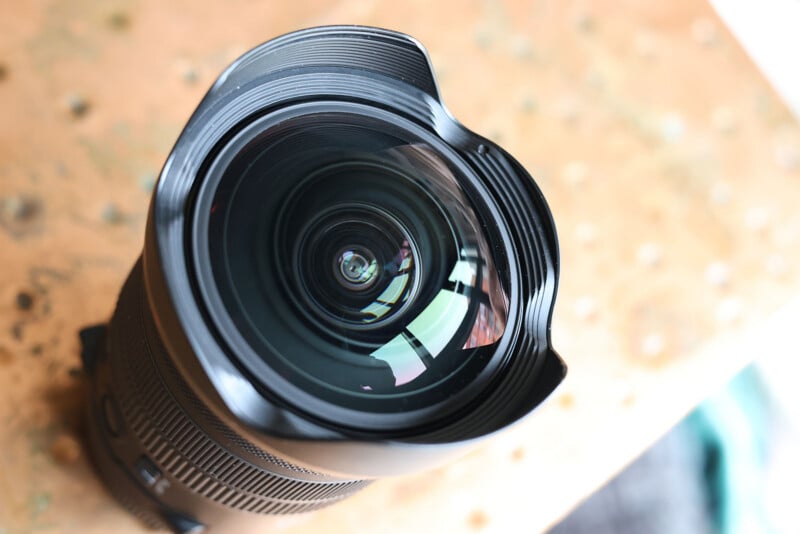 Close-up view of a wide-angle camera lens placed on a wooden surface, showing the intricate layers of glass and the petal-shaped lens hood.