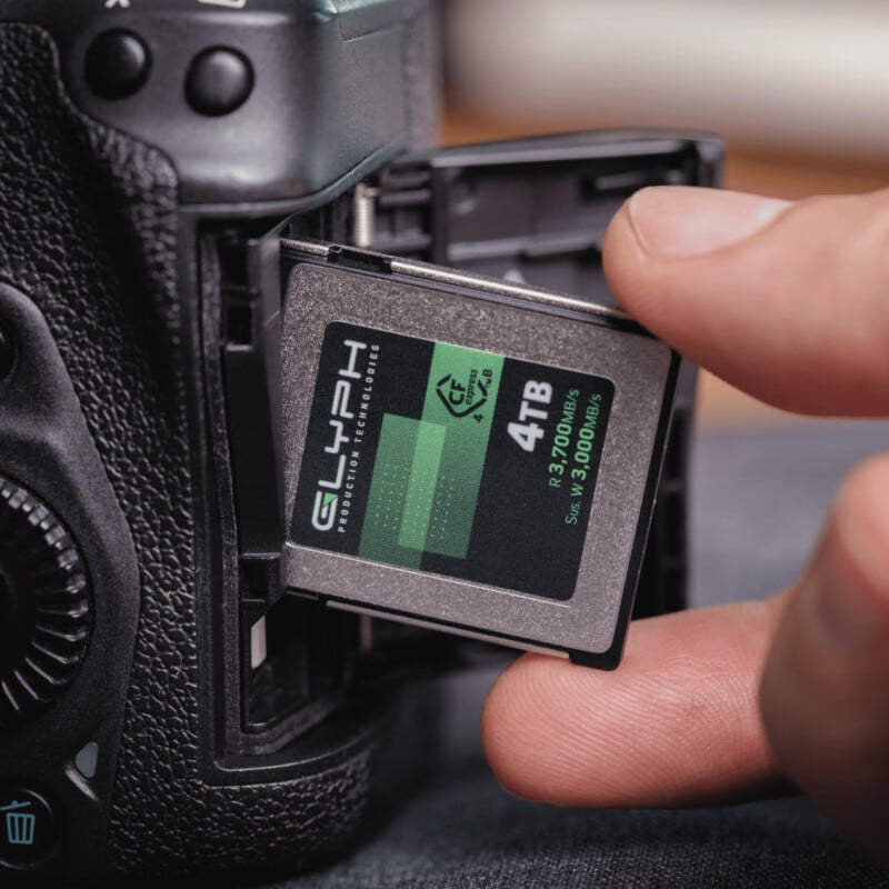 A close-up of a hand inserting a 4TB Glyph memory card into a professional camera’s memory card slot. The camera and the card are both in sharp focus.