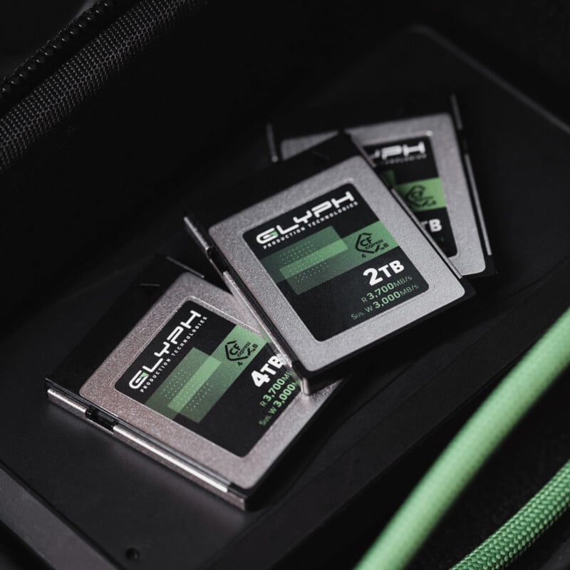 Three Glyph memory cards labeled 2TB, 4TB, and 8TB, partially overlapping each other, are placed on a dark surface with a green zipper visible on the right side of the image.