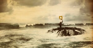 A person in business attire stands on a rocky outcrop surrounded by rough ocean waves under a cloudy sky. The person’s head is replaced by a yellow sign with a white upward arrow.